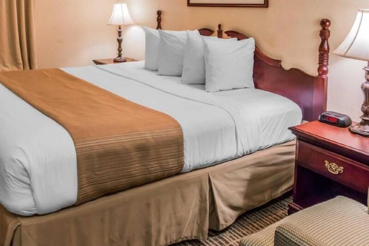 A hotel room with a bed, a nightstand, a lamp, a painting on the wall, and a clock.