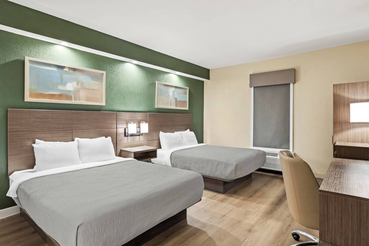 A hotel room with two beds, a desk, a chair, and artwork on the walls.