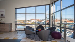 A modern living room with large windows, a view of a cityscape, and a dining area with a wooden cabinet.