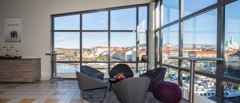 Ein modernes Wohnzimmer mit großen Fenstern, Blick auf eine Stadtlandschaft und einem Essbereich mit einem Holzkabinett.