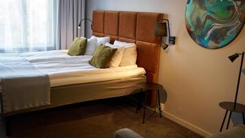 A hotel room with a large bed, a bedside table, a wall-mounted lamp, and a painting.