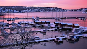 A marina with boats docked, wooden buildings, and a snowy landscape.