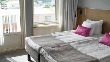 Una habitación de hotel con una cama grande, vistas por la ventana y una mesita de noche con una lámpara.