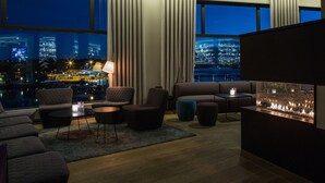 A modern lounge with a city view, comfortable seating, and a fireplace.