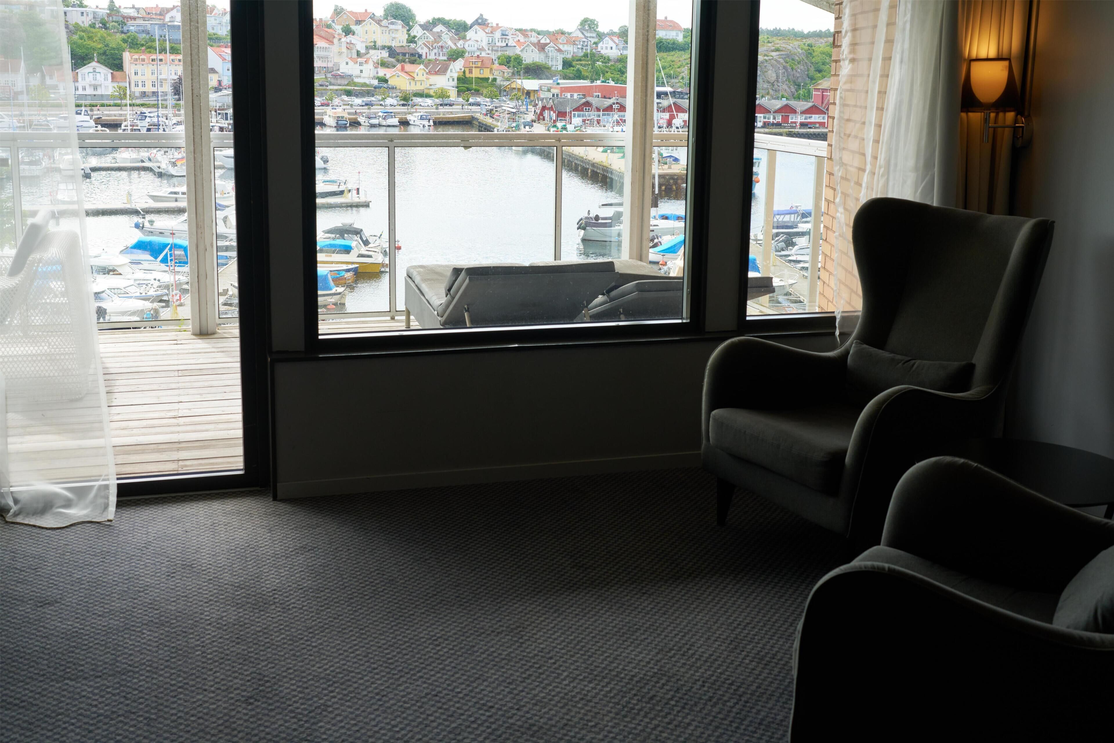 Habitación con un amplio ventanal con vista a un puerto deportivo y al pueblo. Hay dos sillas y una mesita.