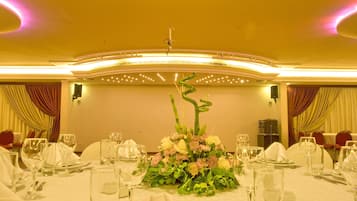 Un salón de banquetes con mesas redondas dispuestas para cenar, con centros de mesa florales y un techo alto con iluminación empotrada.