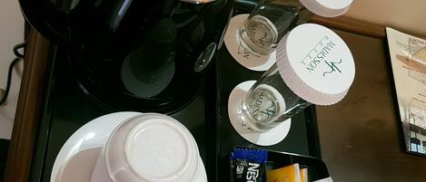 Een koffiezetapparaat, een glas water, een kop, een bord en een pakje Nescafe koffie op een dienblad.