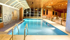 Une piscine intérieure avec des parois en verre transparent, un plafond en bois et une fresque murale.