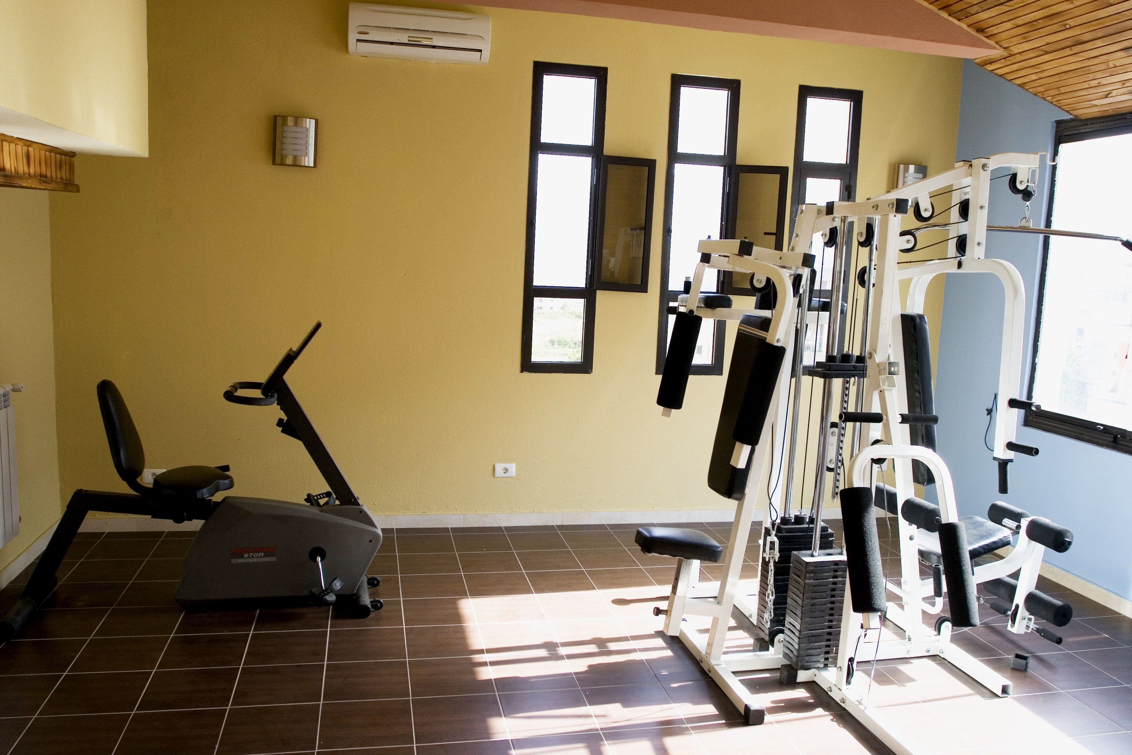 Une salle de sport équipée de matériel d’exercice, d’un tapis de course et d’une fenêtre avec des stores.