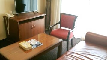 A hotel room with a leather sofa, a wooden coffee table, a television on a wooden cabinet, and a red chair.