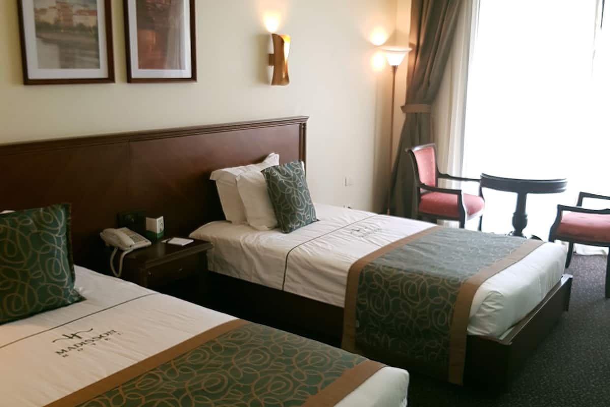 A hotel room with two beds, a desk, a chair, and a lamp.