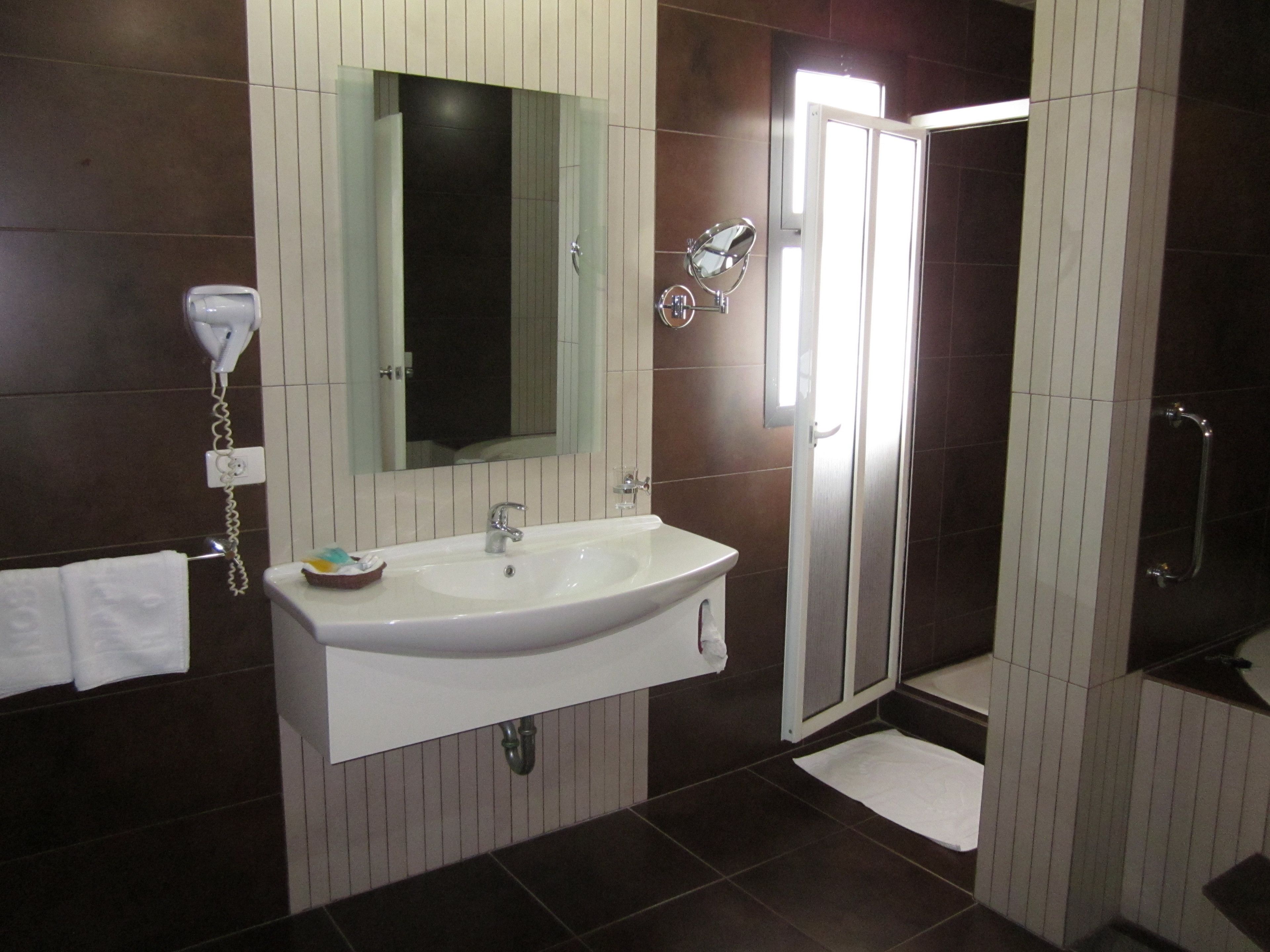 A bathroom with a white sink, a mirror, a hairdryer, and a shower area.