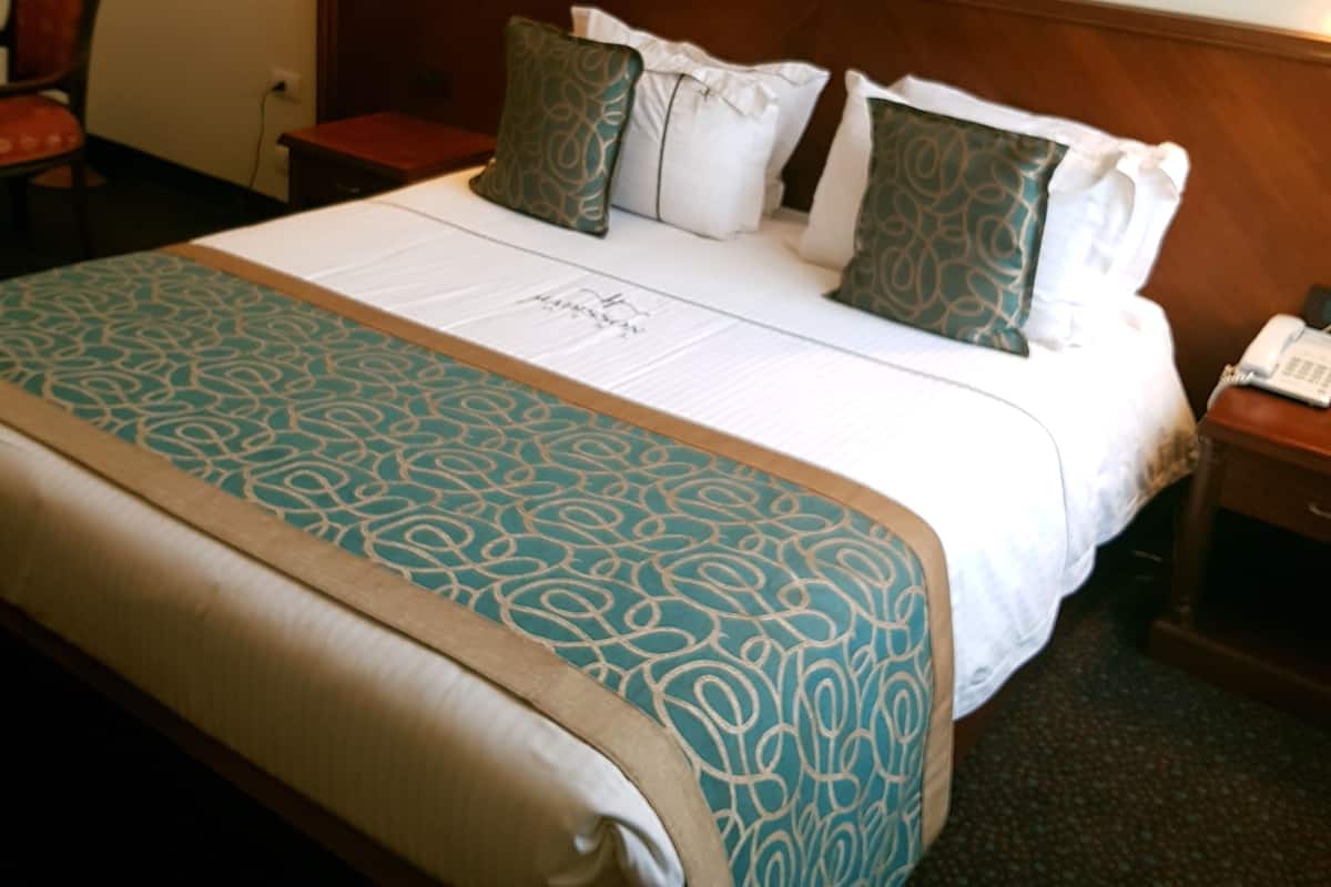A hotel room with a large bed, a nightstand, a chair, and two framed pictures on the wall.