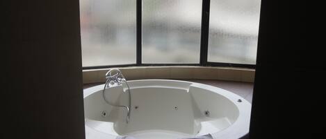 A bathtub with a showerhead, a towel, and a window with frosted glass.