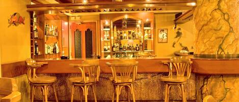 Zona de bar con taburetes de madera, barra y estanterías llenas de botellas.
