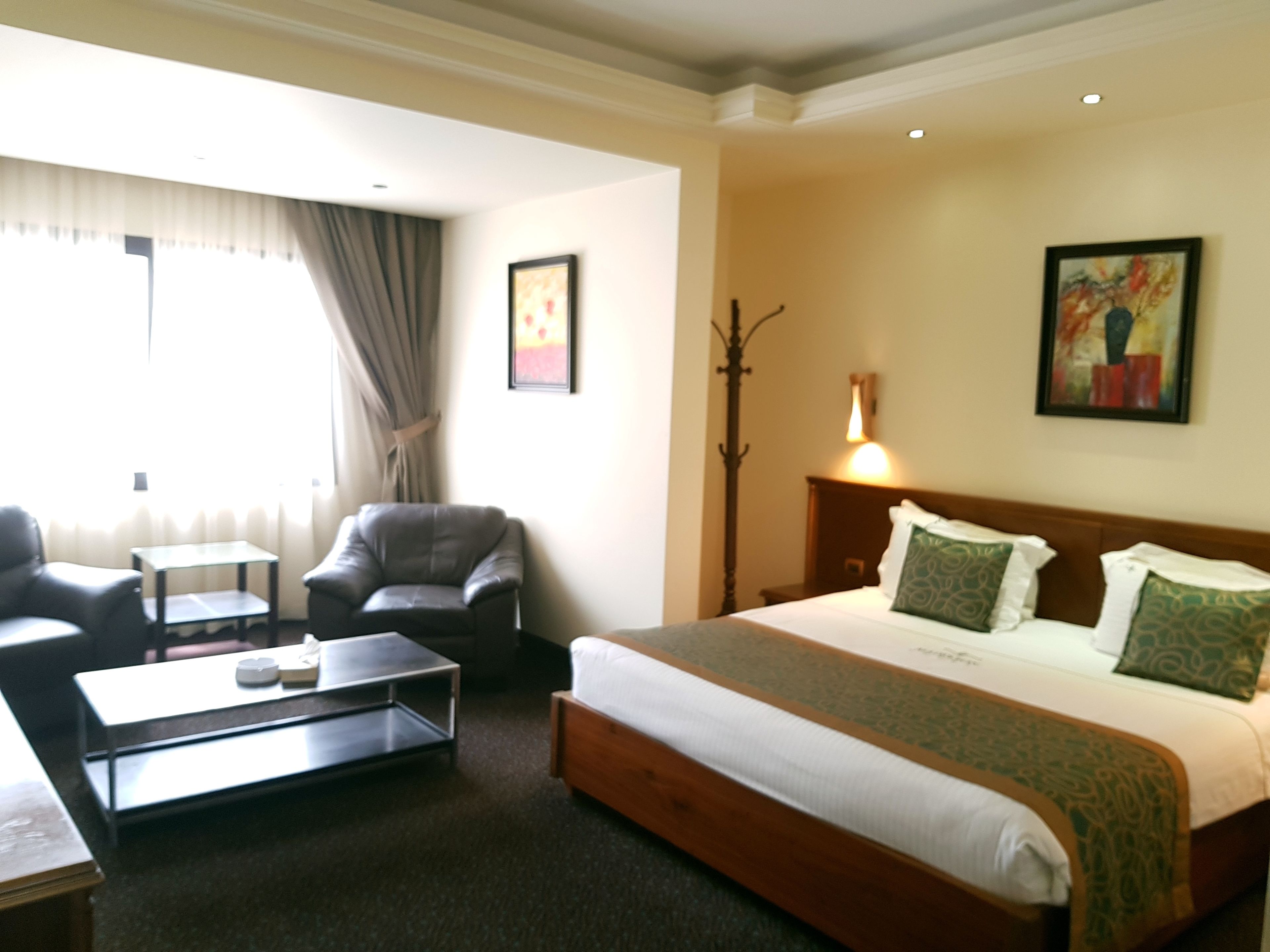 Habitación de hotel con cama, escritorio, silla, lámpara y un cuadro en la pared.