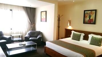 Habitación de hotel con cama, escritorio, silla, lámpara y un cuadro en la pared.