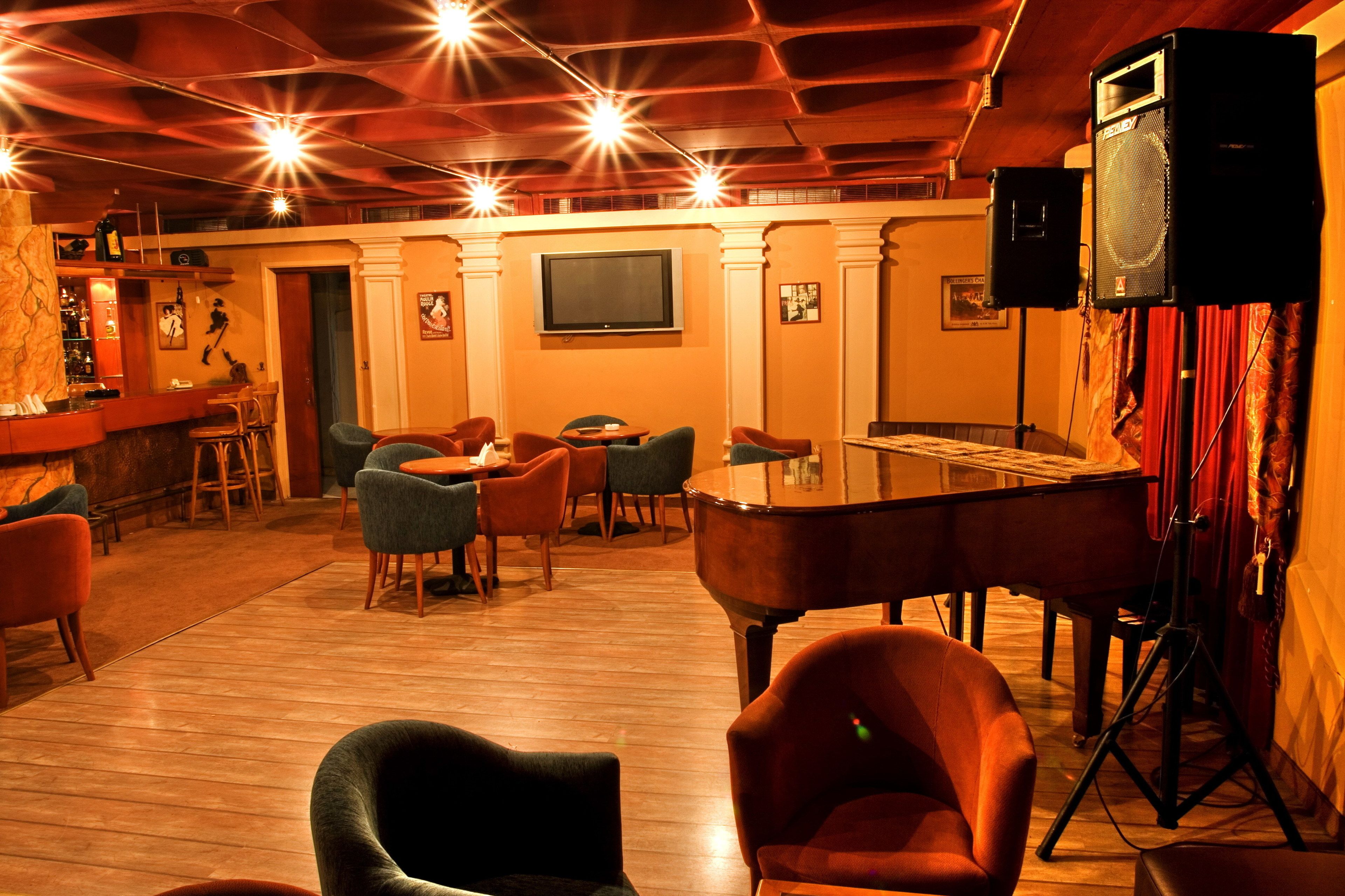 A cozy bar area with wooden flooring, comfortable seating, a piano, and a television screen.