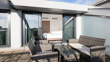 Uma área externa moderna com mobiliário de vime e uma porta de vidro que dá para um quarto.