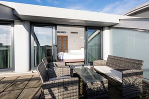 A modern outdoor seating area with wicker furniture and a glass door leading to a bedroom.