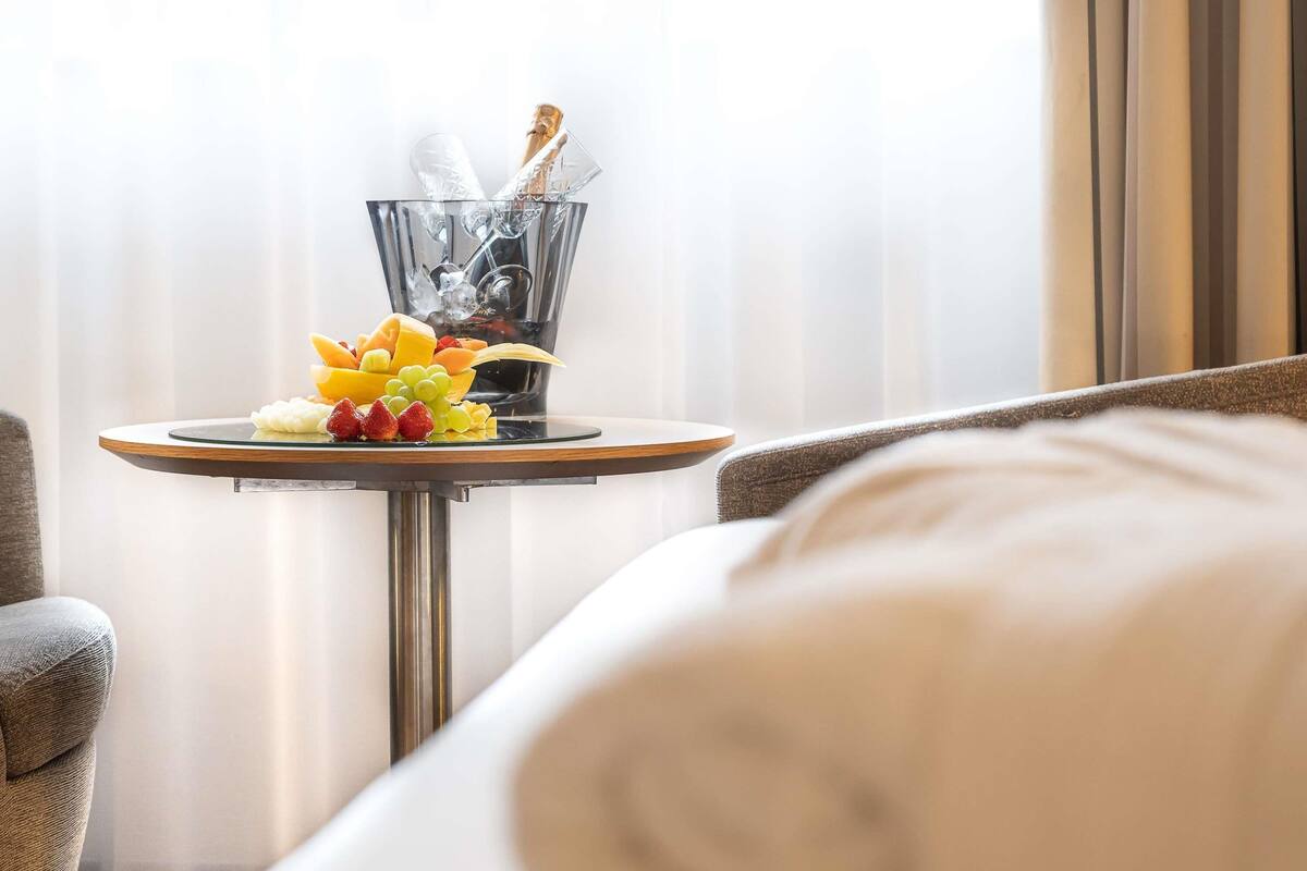 A hotel room with a round table featuring a fruit platter and a champagne bottle.