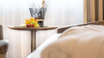 Quarto de hotel com uma mesa redonda, um prato de frutas e uma garrafa de champanhe.