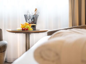 A hotel room with a round table featuring a fruit platter and a champagne bottle.