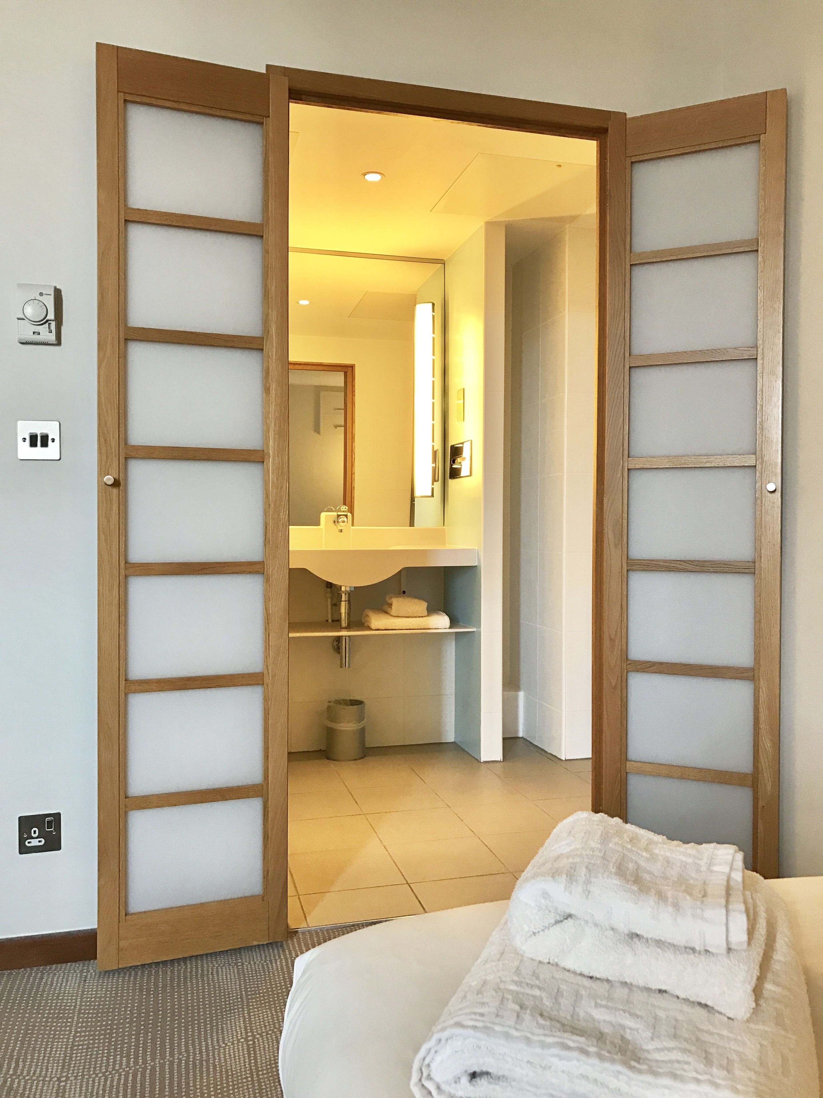 A hotel room with a wooden door, a sink, a mirror, and a bed with a towel.