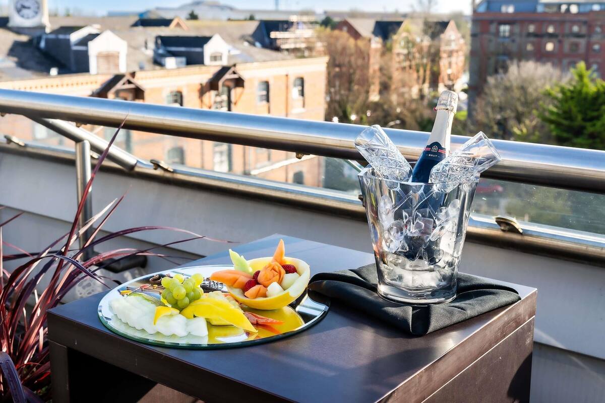 A balcony with a table set with fruit and a bottle of Brut champagne, overlooking a cityscape.