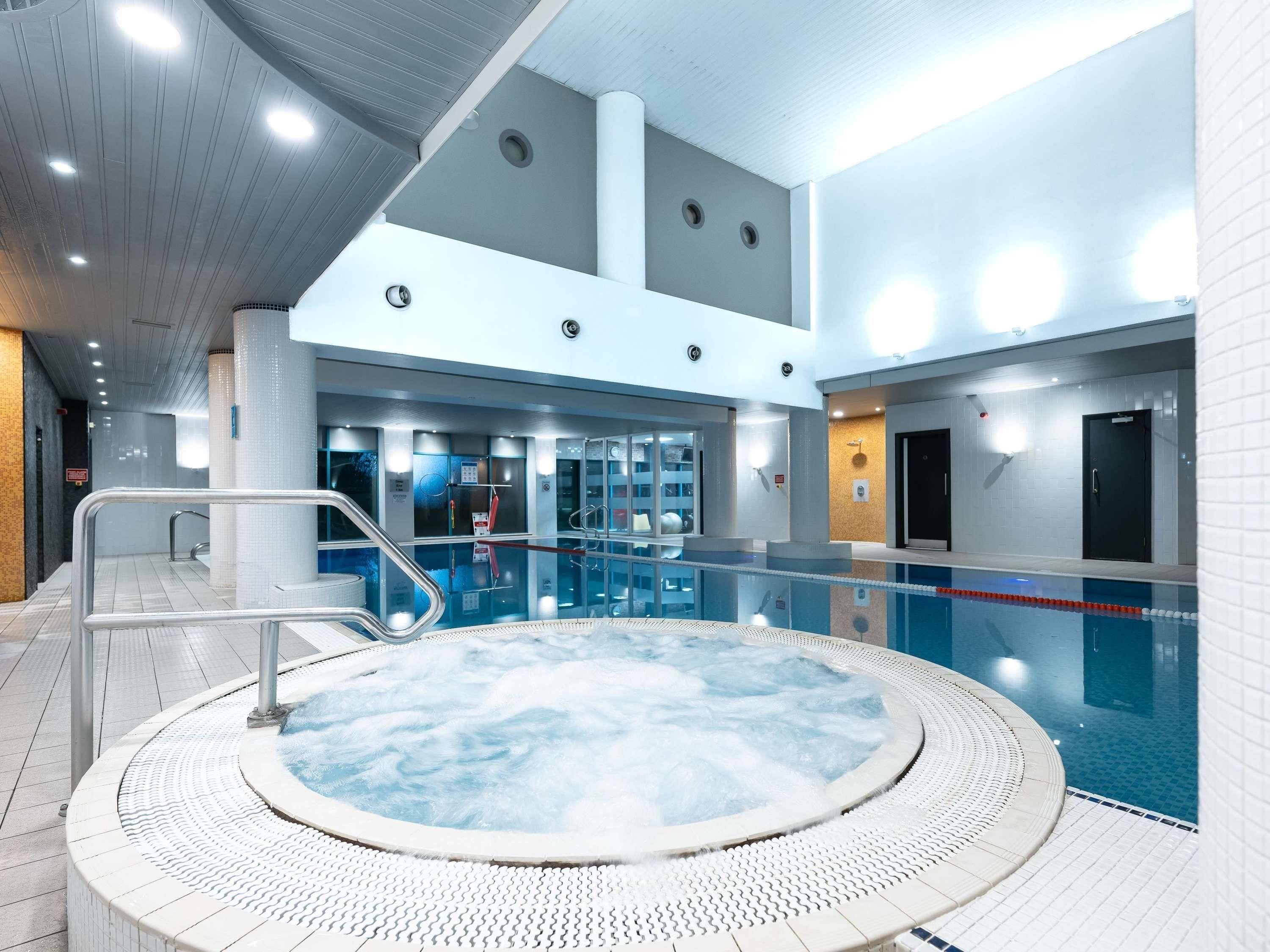 A modern indoor swimming pool with a hot tub, clear water, and a tiled floor.