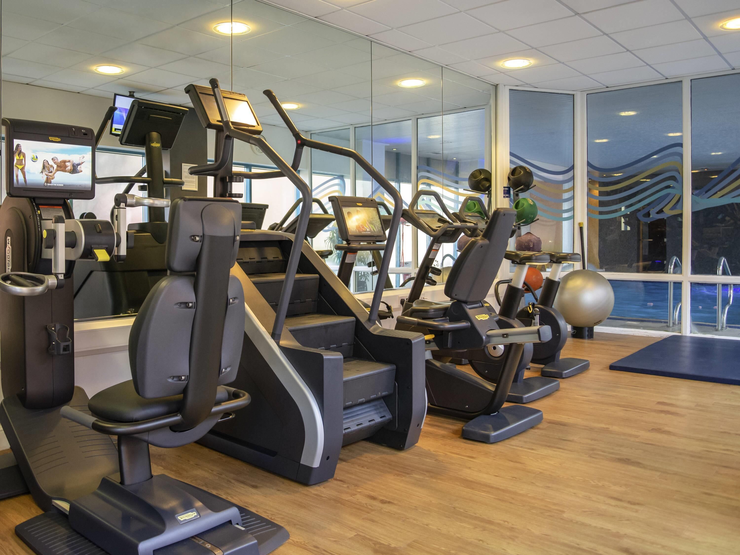 A gym with treadmills, exercise bikes, and a TV screen displaying fitness content.