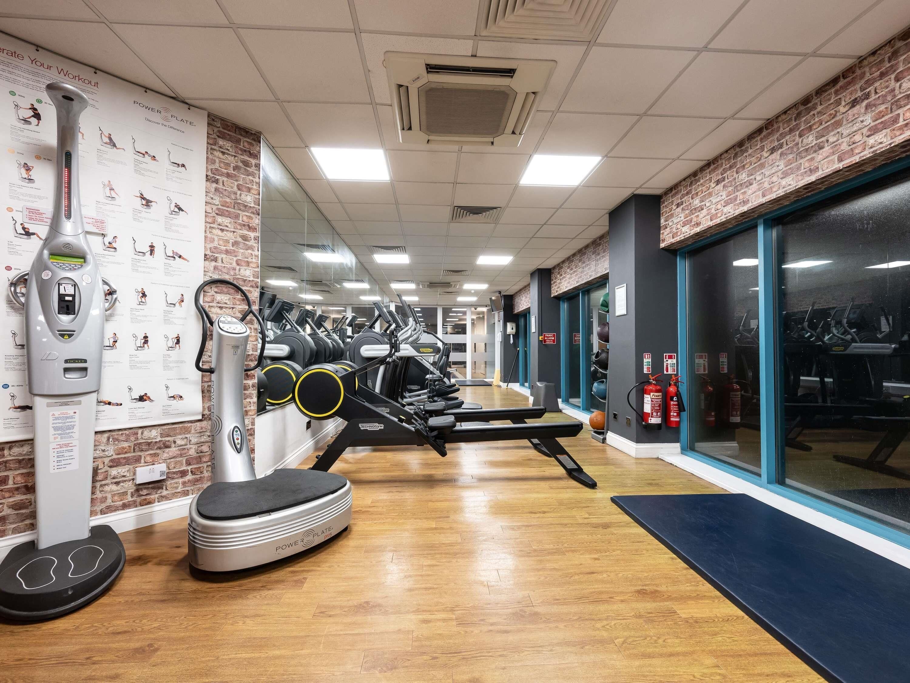 A gym with exercise equipment, a mirrored wall, and a brick wall.
