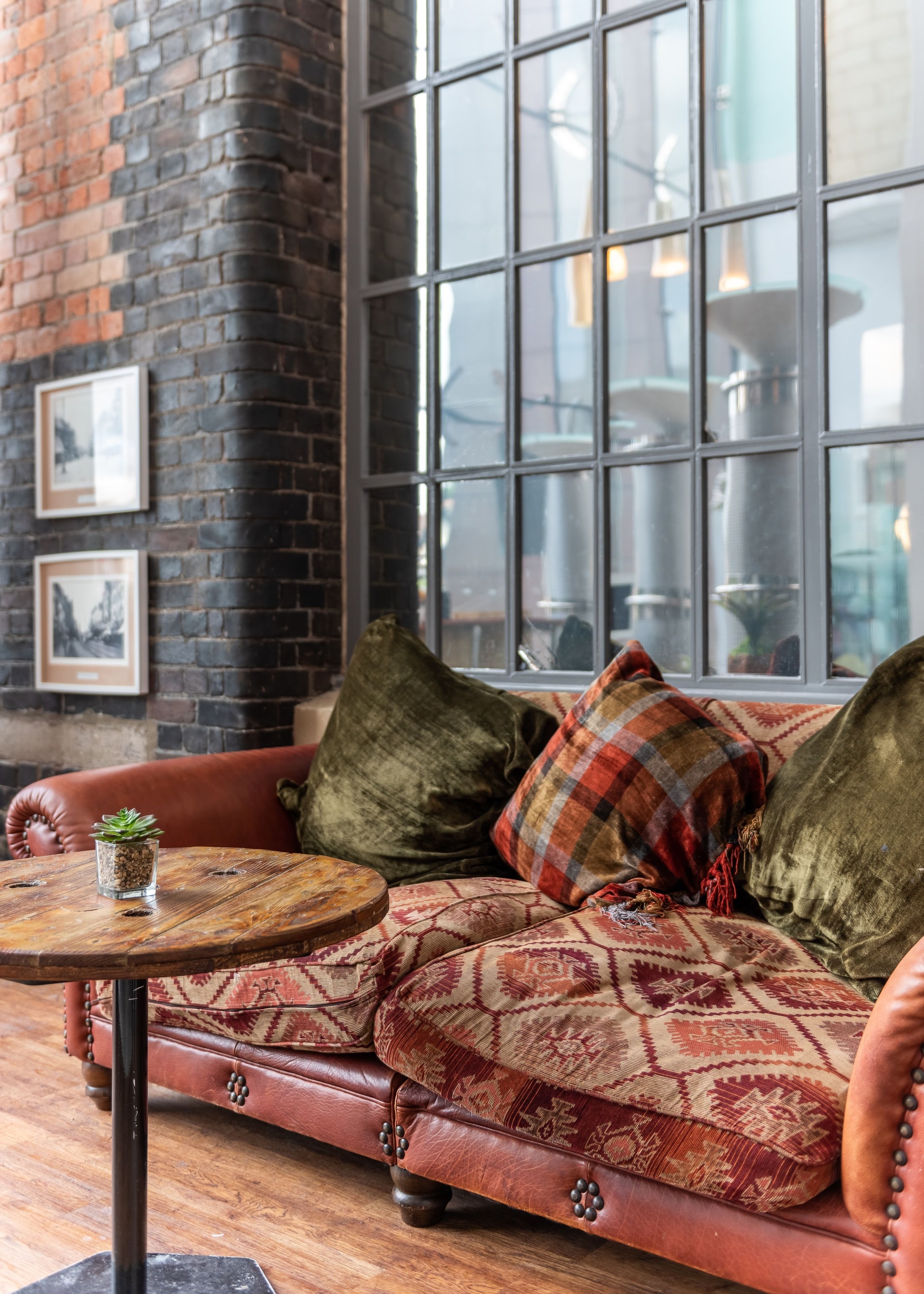 A cozy seating area with a leather sofa, a round wooden table, and a brick wall with framed pictures.