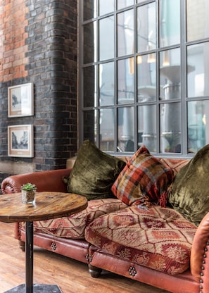 A cozy seating area with a leather sofa, a round wooden table, and a brick wall with framed pictures.