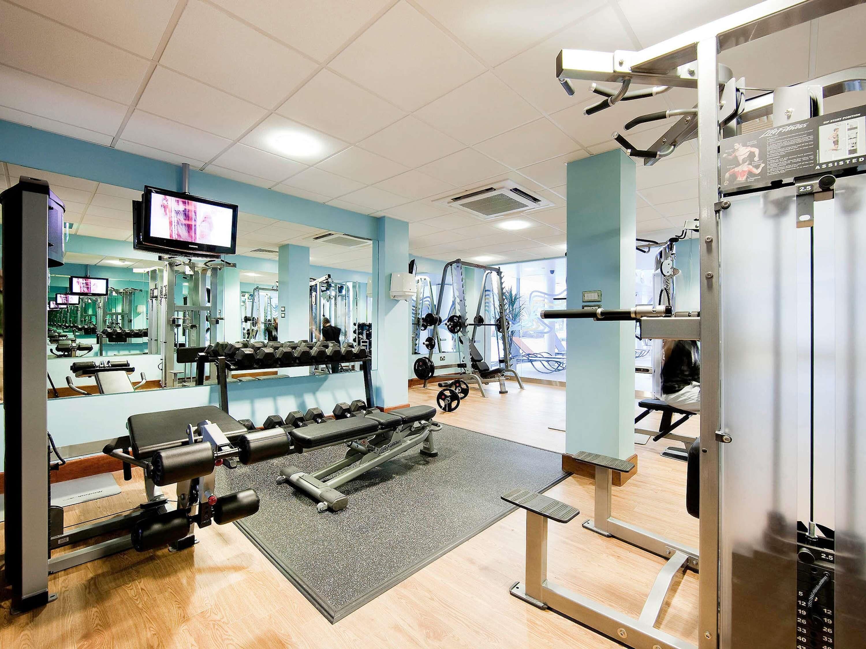 A gym with exercise equipment, mirrors, and a television screen.