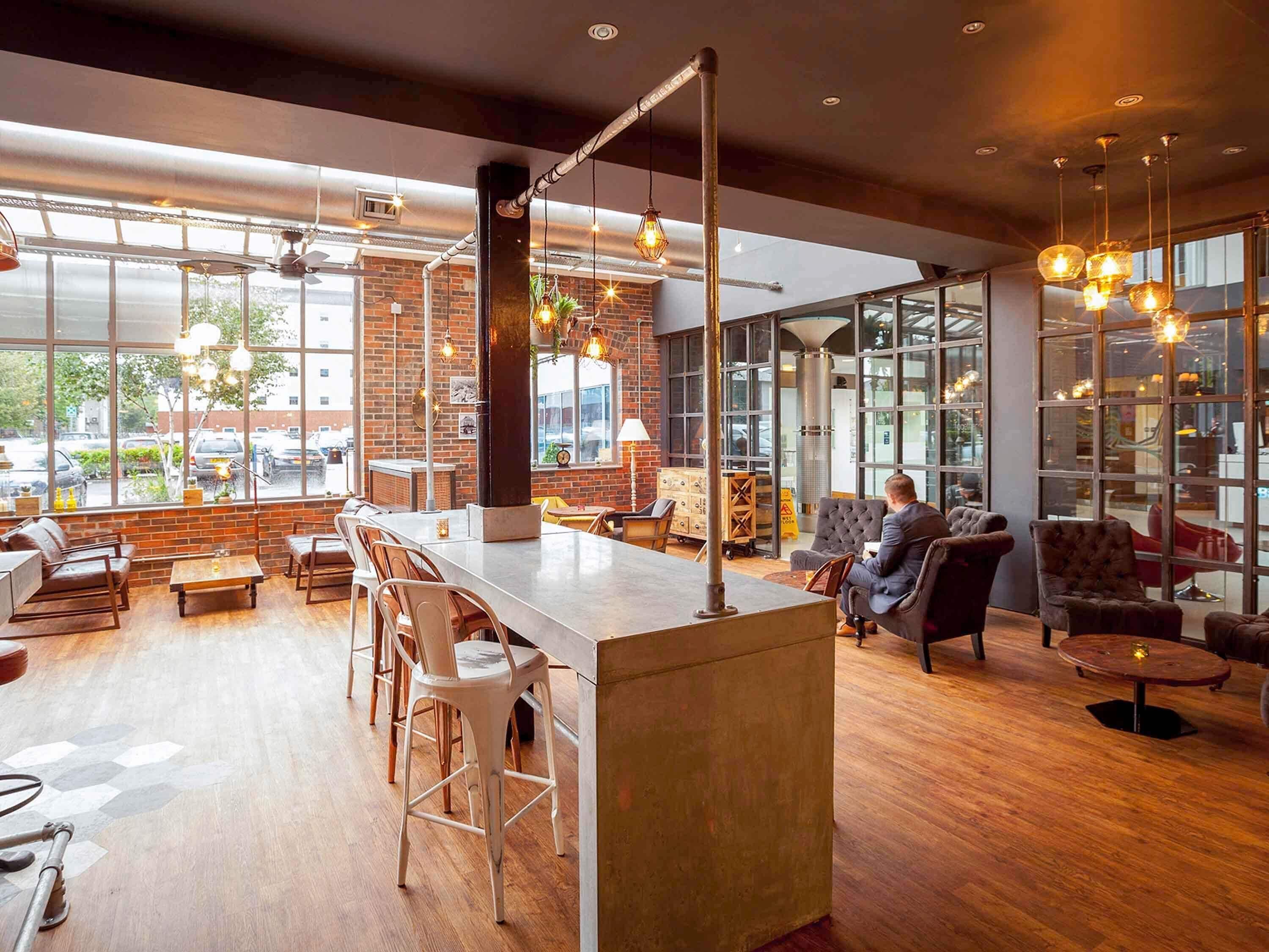 A spacious bar area with seating, large windows, and a brick wall.