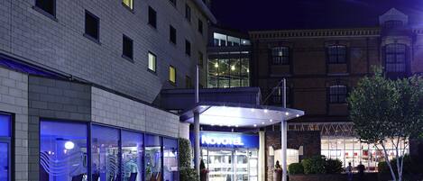 A hotel entrance with a modern facade, large glass windows, and a prominent 'NOVOTEL' sign.