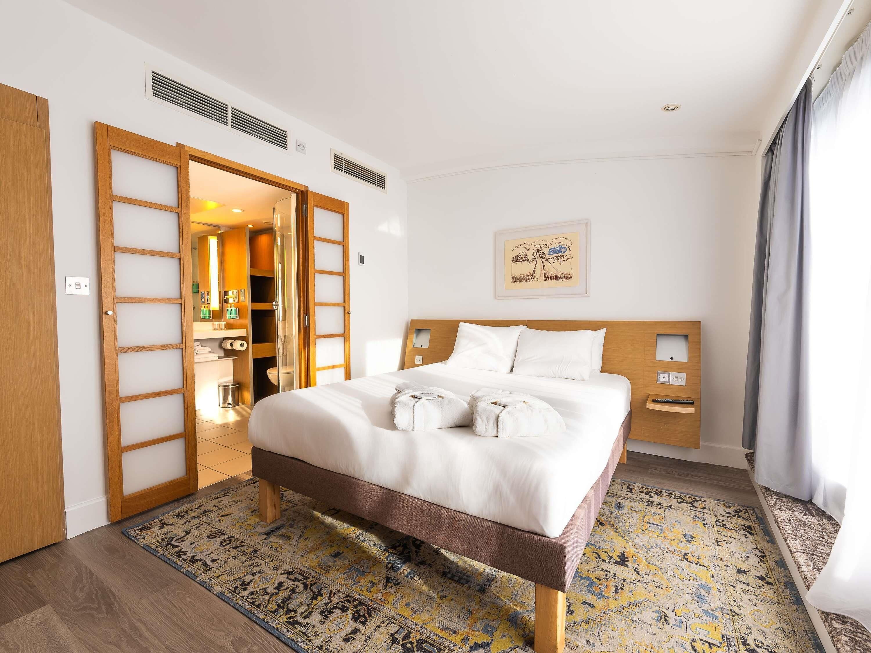A hotel room with a bed, a wardrobe, a bathroom, and a painting on the wall.