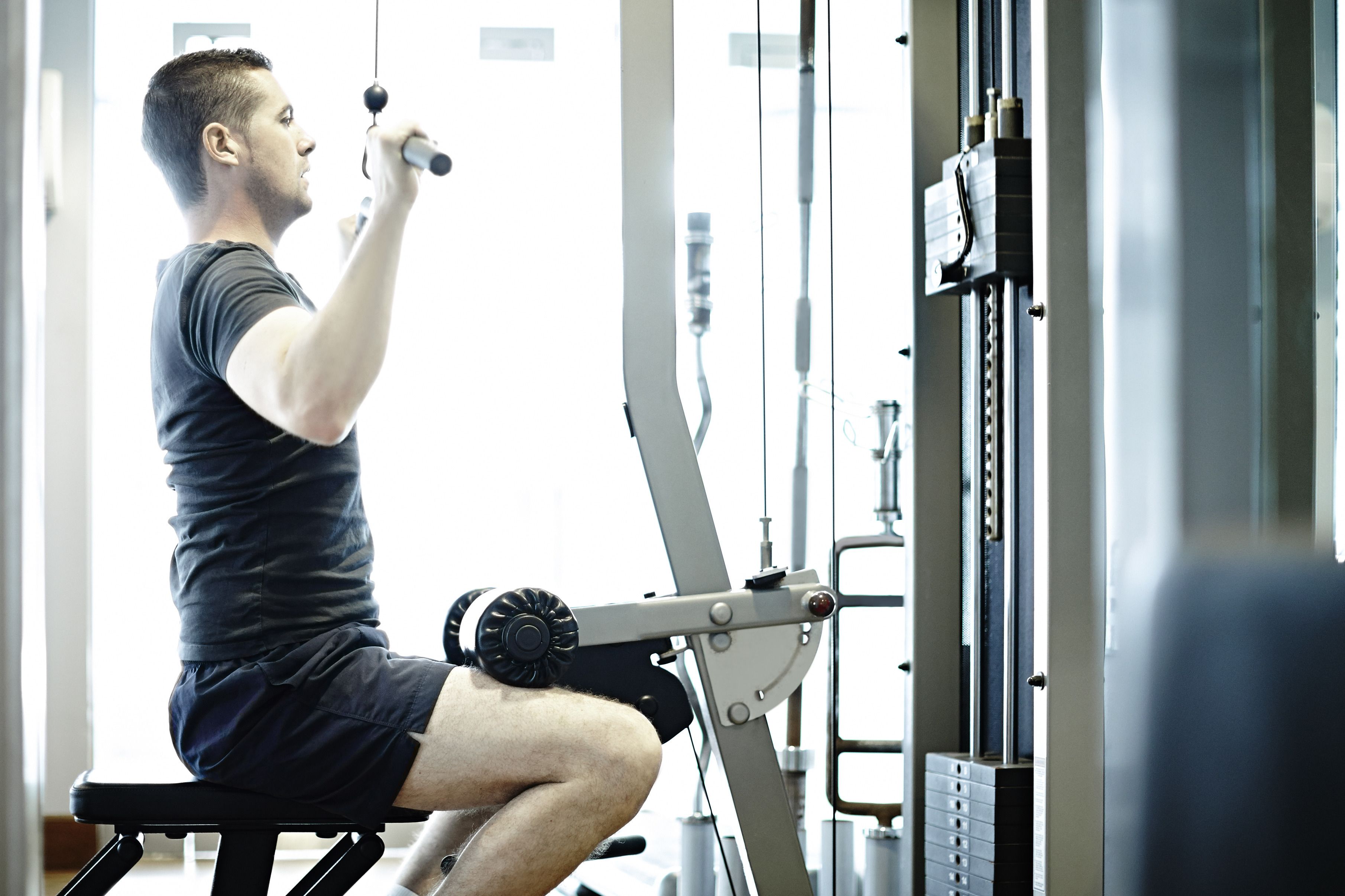 En person bruger et kabeltræningsapparat i et fitnesscenter.