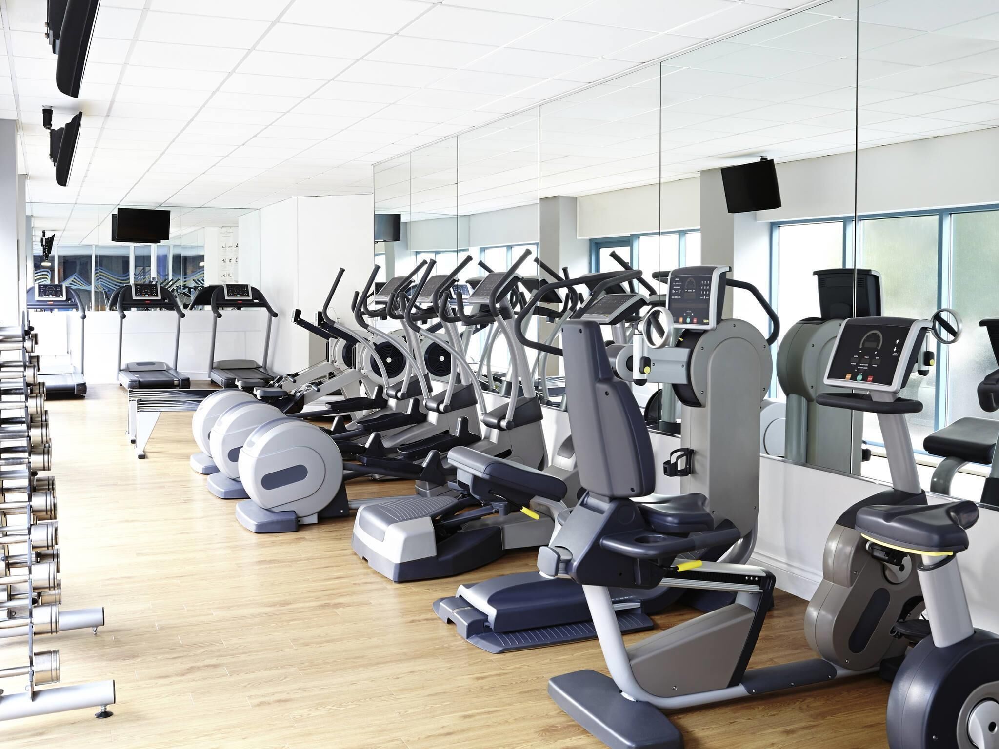 Een sportschool met diverse fitnessapparaten, waaronder loopbanden, crosstrainers en hometrainers.