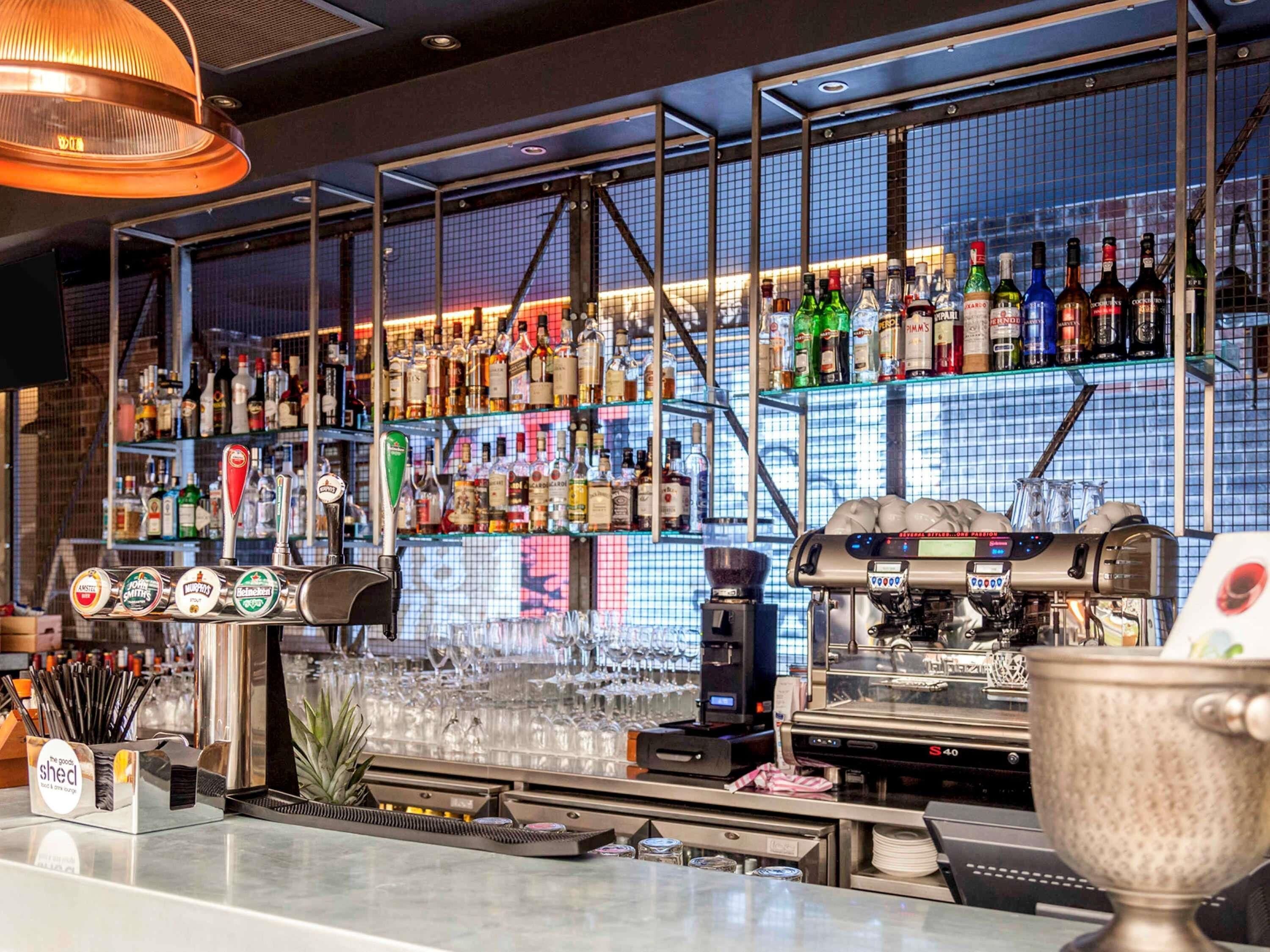 Un bar con una variedad de botellas de licor, una máquina de café y una vitrina con cristalería.
