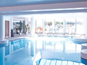 A swimming pool with lounge chairs and potted plants, surrounded by large windows. - Novotel Cardiff Centre (Cardiff)