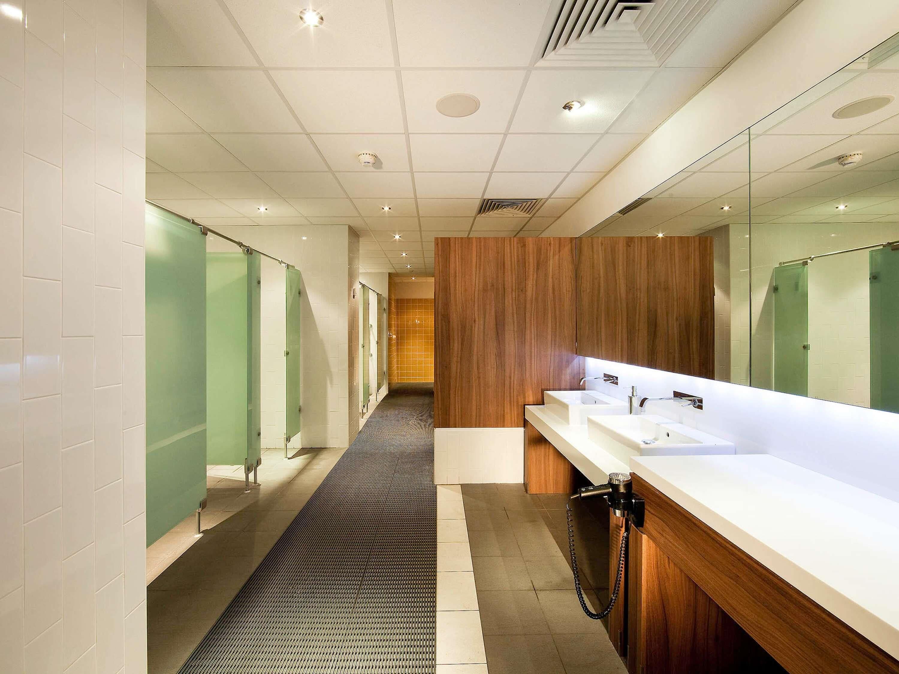 A modern bathroom with a long corridor, individual stalls, a vanity area with sinks, and a wooden accent wall.