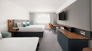 Une chambre d’hôtel avec deux lits, un bureau, une chaise, un téléviseur fixé au mur et une fenêtre avec des rideaux.