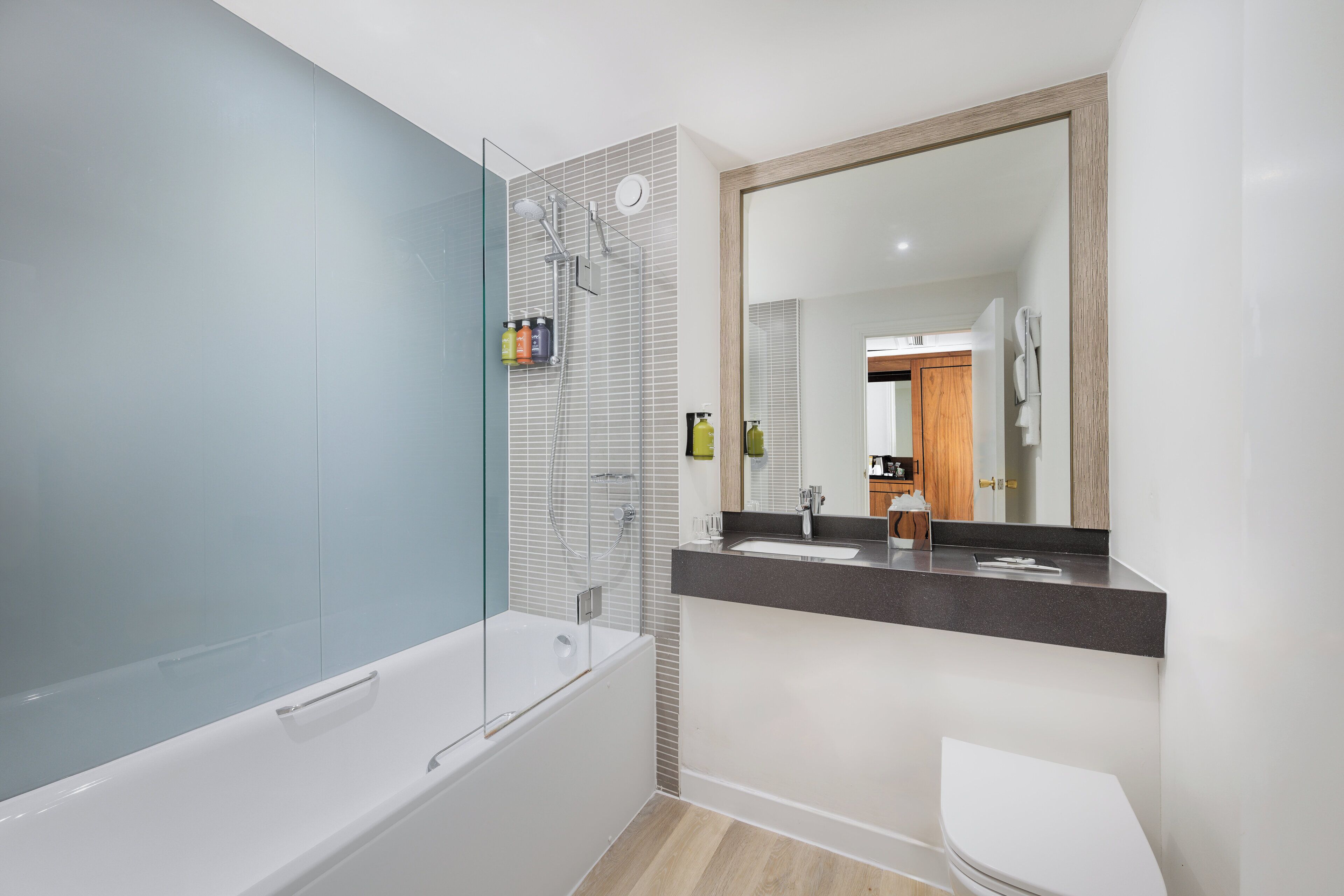 A modern bathroom with a glass-enclosed shower, a white bathtub, a sink with a dark countertop, and a large mirror.