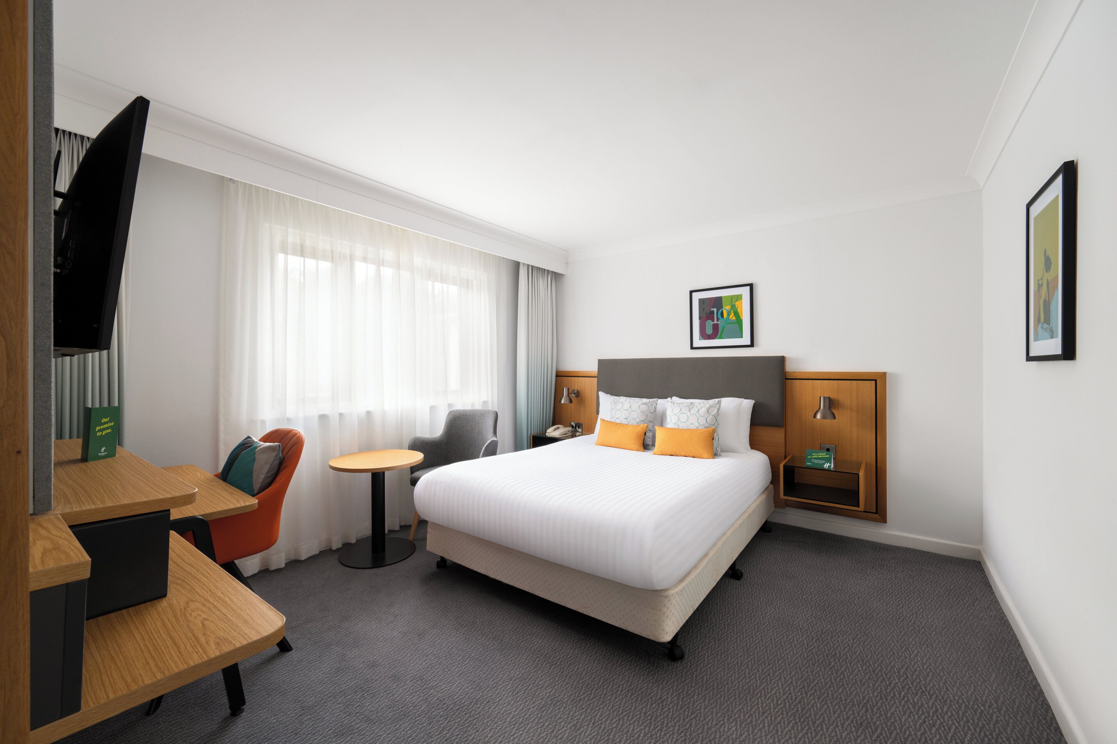 Habitación de hotel con cama, escritorio, silla, televisor y ventana con cortinas.