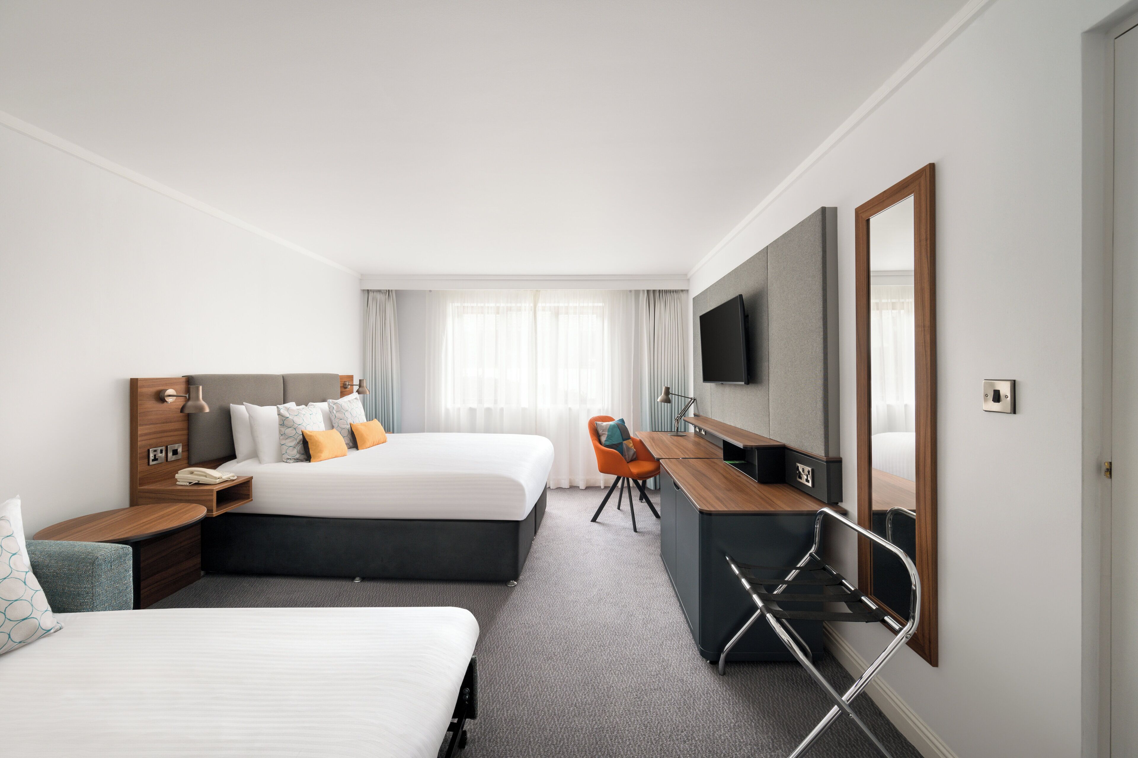 Une chambre d’hôtel avec deux lits, un bureau, une télévision et un miroir.