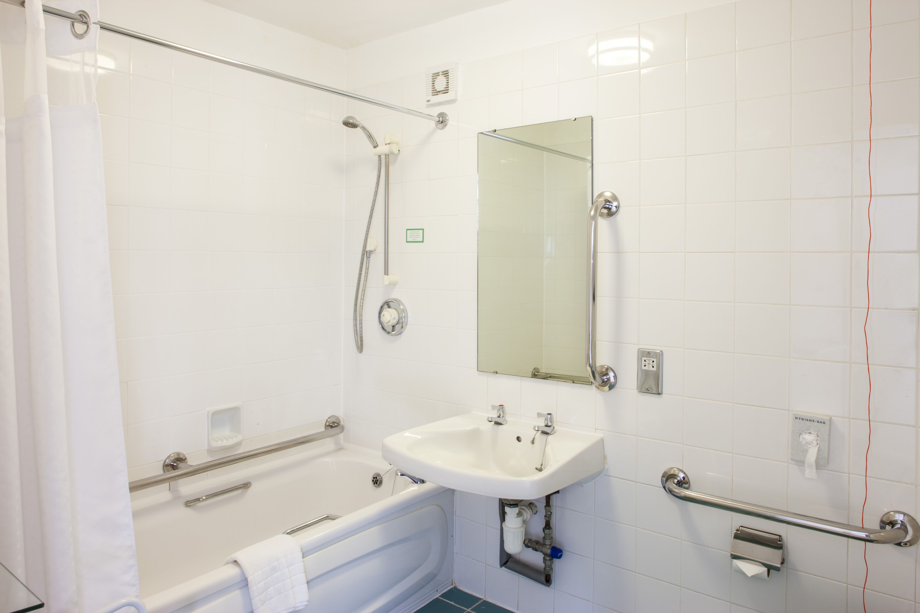 A bathroom with a bathtub, a sink, a mirror, and a shower with a grab bar.