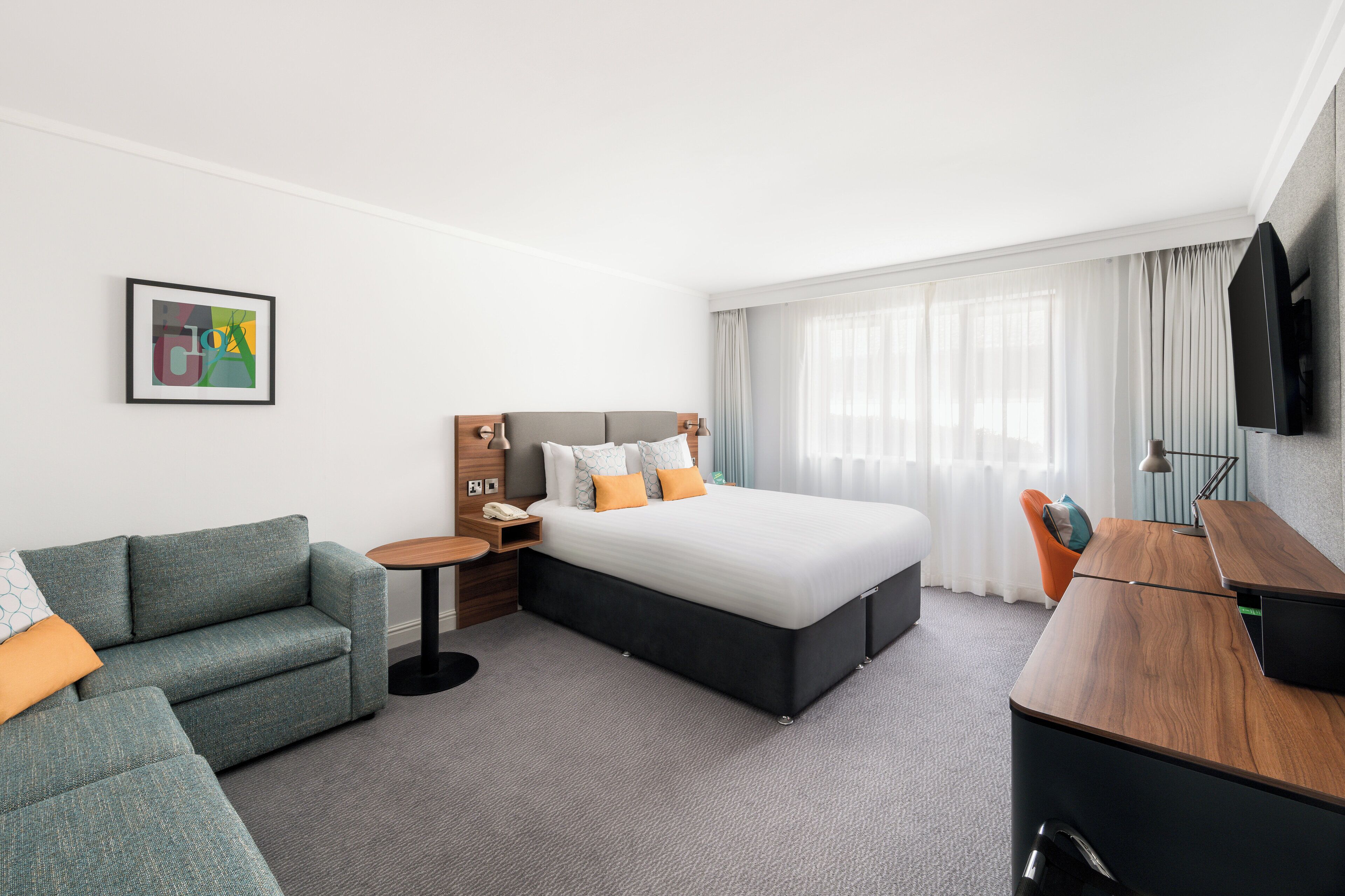 A hotel room with a bed, a sofa, a desk, and a TV.