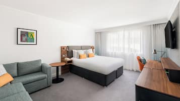 A hotel room with a bed, a sofa, a desk, and a TV.